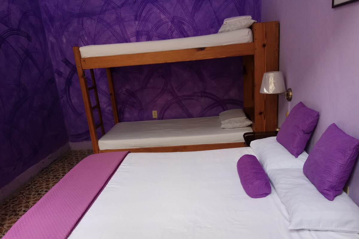 A bunk bed with a wooden frame, white bedding, and purple pillows.