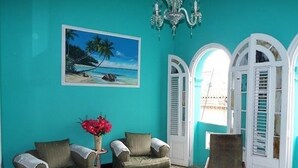 A room with teal walls, a beach painting, a chandelier, and a patterned carpet. - Hostal Casa de Alexis y Mary (Havana)