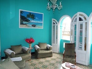 A room with teal walls, a beach painting, a chandelier, and a patterned carpet. - Hostal Casa de Alexis y Mary (Havana)