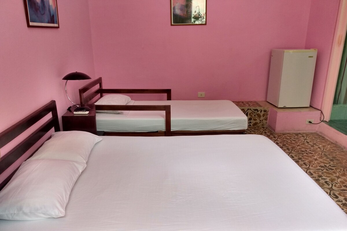 A room with two beds, a desk, a lamp, and a refrigerator.