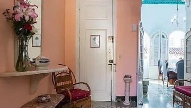 A room with a patterned floor, a white door, a mirror, a vase with flowers, and wicker furniture. - Hostal Casa de Alexis y Mary (Havana)