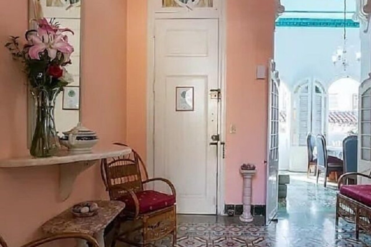 A room with a patterned floor, a white door, a mirror, a vase with flowers, and wicker furniture.