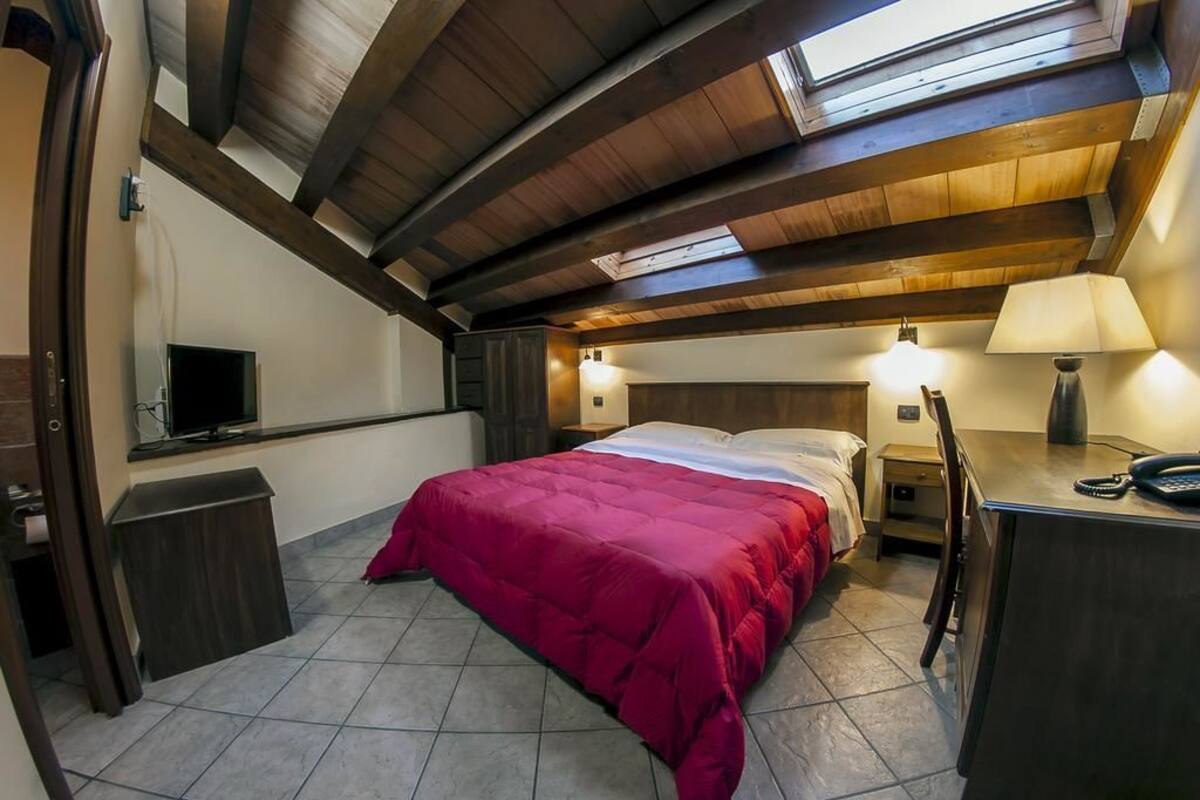 A bedroom with a bed, bedside tables, a desk, a lamp, and a television.
