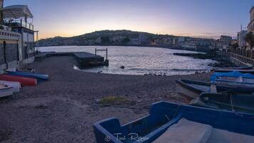 Boats docked on a pebbled beach, overlooking a calm body of water.