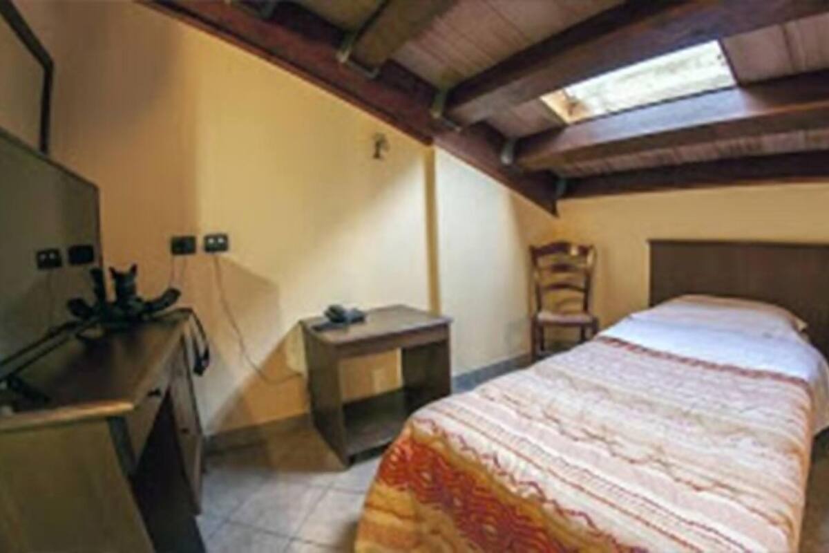 A bedroom with a bed, a desk, a chair, a TV, and a window.