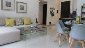 En moderne stue med et glasbord, en grå sofa og et spiseområde med stole og et lille bord.