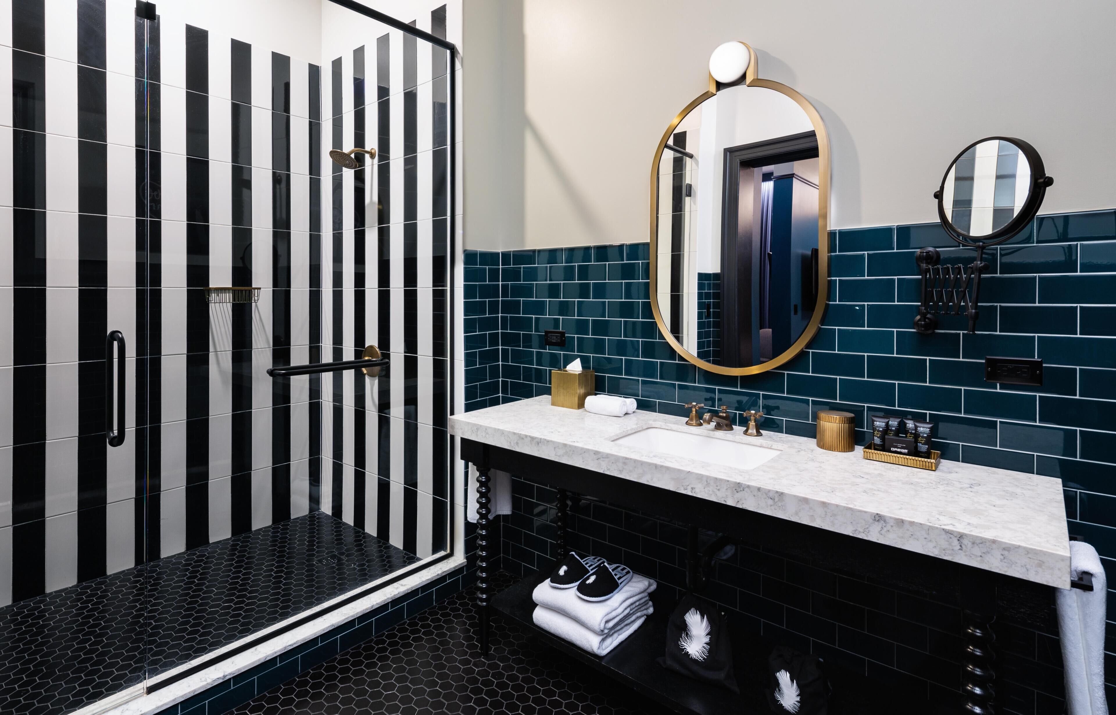 A modern bathroom with a black and white striped shower, a white sink with gold fixtures, and a large mirror.