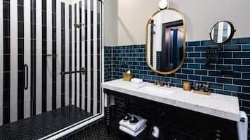 A modern bathroom with a black and white striped shower, a white sink with gold fixtures, and a large mirror.