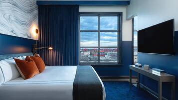 A hotel room with a large bed, a desk, a TV, and a window with a city view.