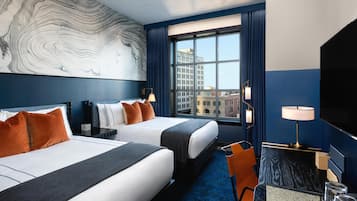 A hotel room with two beds, a large window with a city view, a desk with a lamp, and a wall with a marble-like design.