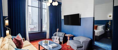 A hotel room with a sofa, armchair, coffee table, and a TV mounted on the wall.