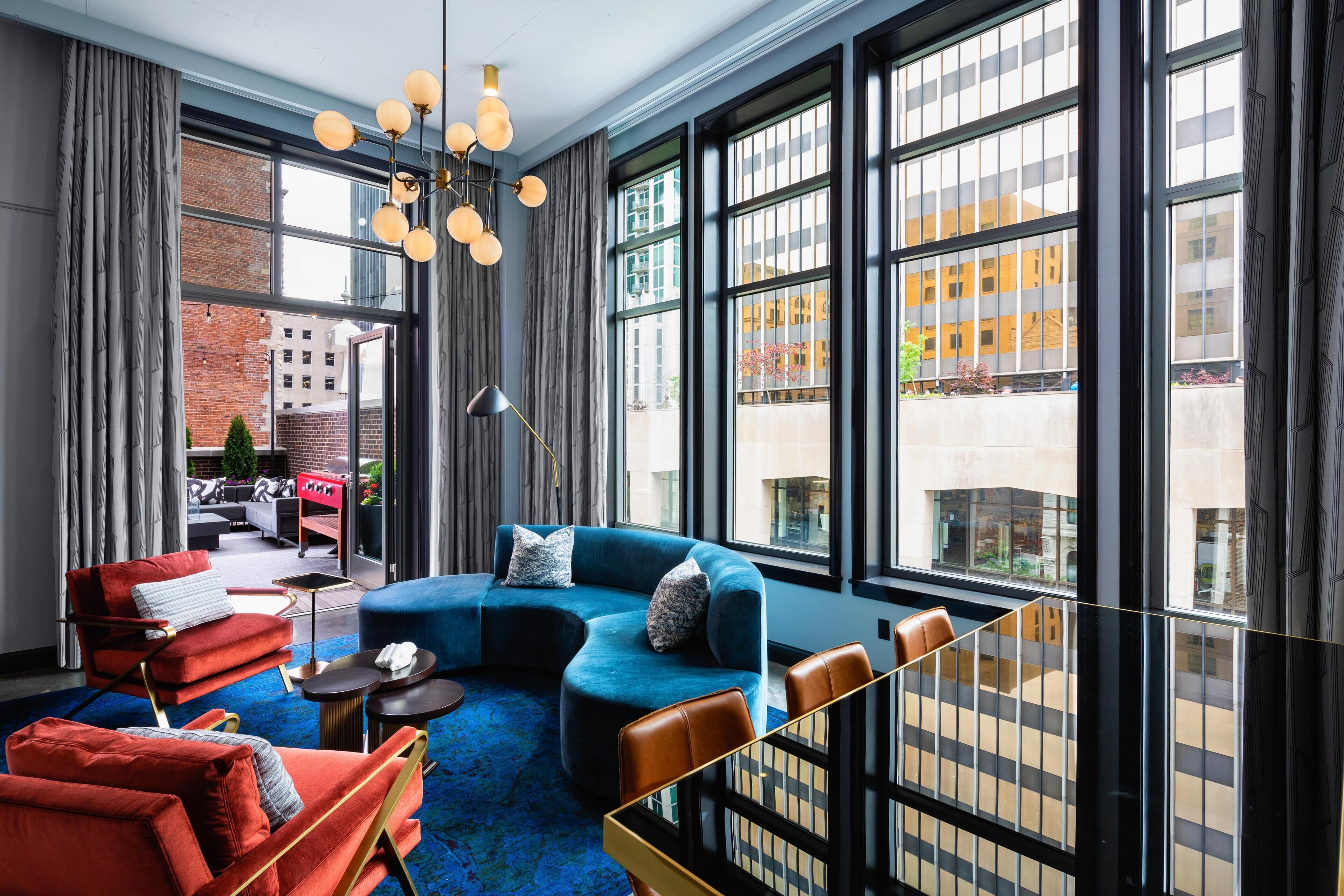 A modern living room with a blue sofa, red armchairs, and a large window with a city view.