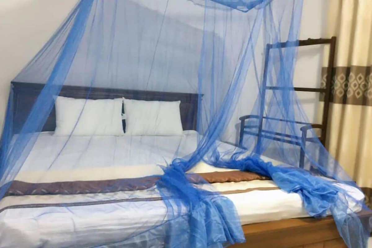 A bed with a blue mosquito net, white pillows, and a wooden headboard.