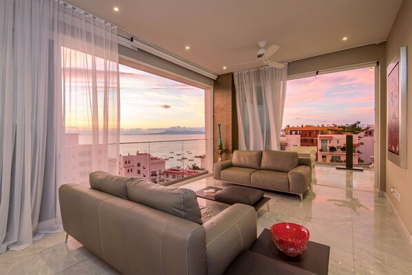 Un salon moderne avec un canapé, une table basse et une vue sur la mer et les bâtiments.