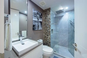 Une salle de bain moderne avec un grand miroir, un lavabo blanc, des toilettes et une douche séparée par une paroi de verre.