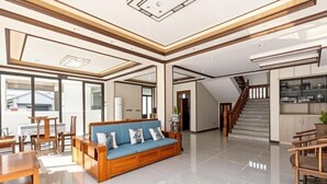 A spacious living area with a wooden sofa, a dining table, and a staircase leading to an upper floor. - Zhouzhuang Yuesheng Hotel (Kunshan)