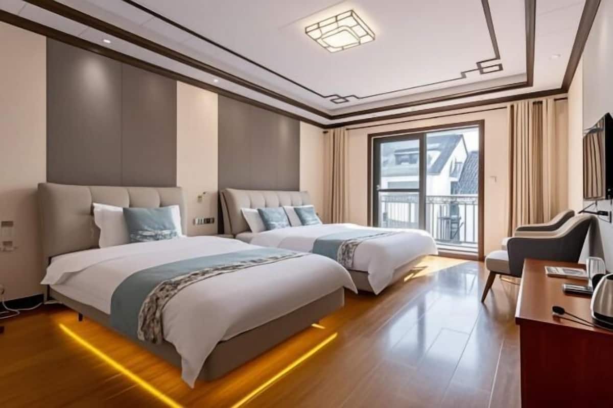 A hotel room with two beds, a desk, and a large window.