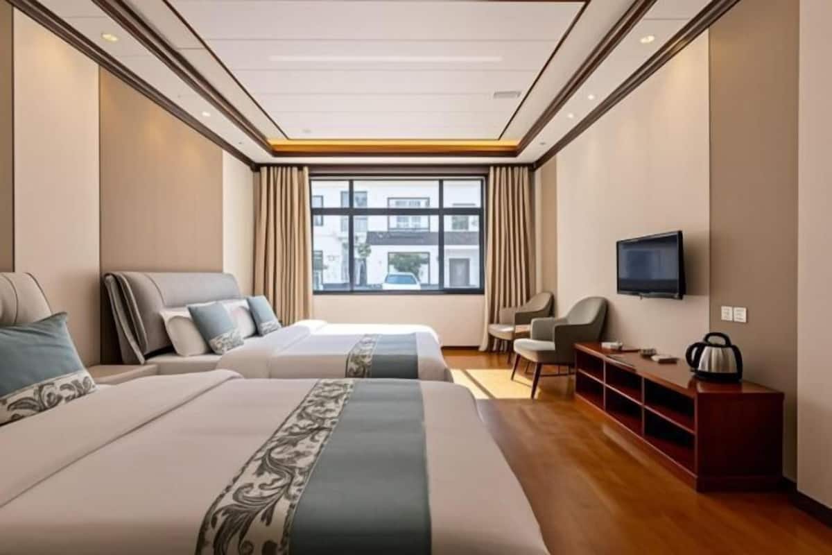 A hotel room with two beds, a TV, a desk, and a window with curtains.