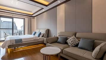 A modern hotel room with a bed, a sofa, a small round table, and a large window offering a view of the outside.