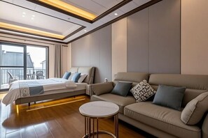 Una habitación de hotel moderna con cama, sofá, una mesita redonda y un ventanal con vistas al exterior.