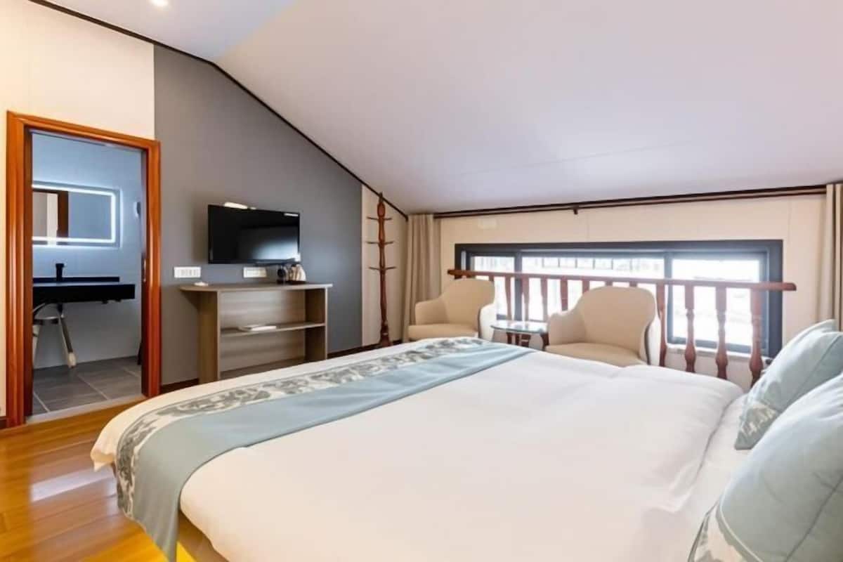 A bedroom with a bed, a desk, a chair, a TV, and a window with a view.