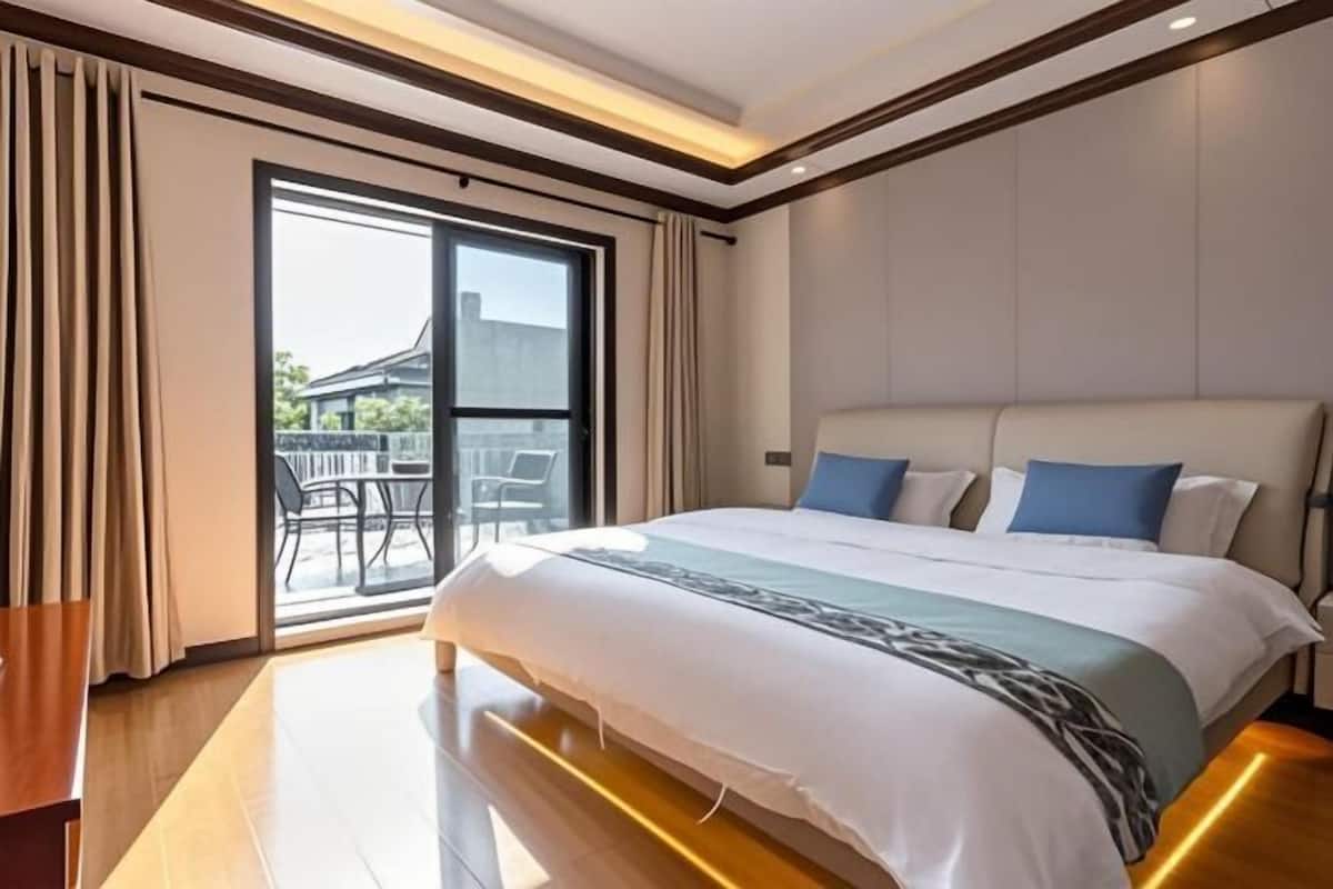 A hotel room with a large bed, a sliding glass door to the balcony, and a wooden floor.