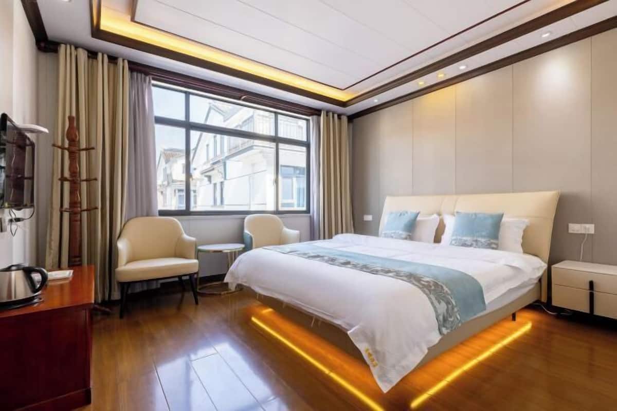 A hotel room with a large bed, a small table, a chair, a coffee maker, and a view of buildings through the window.