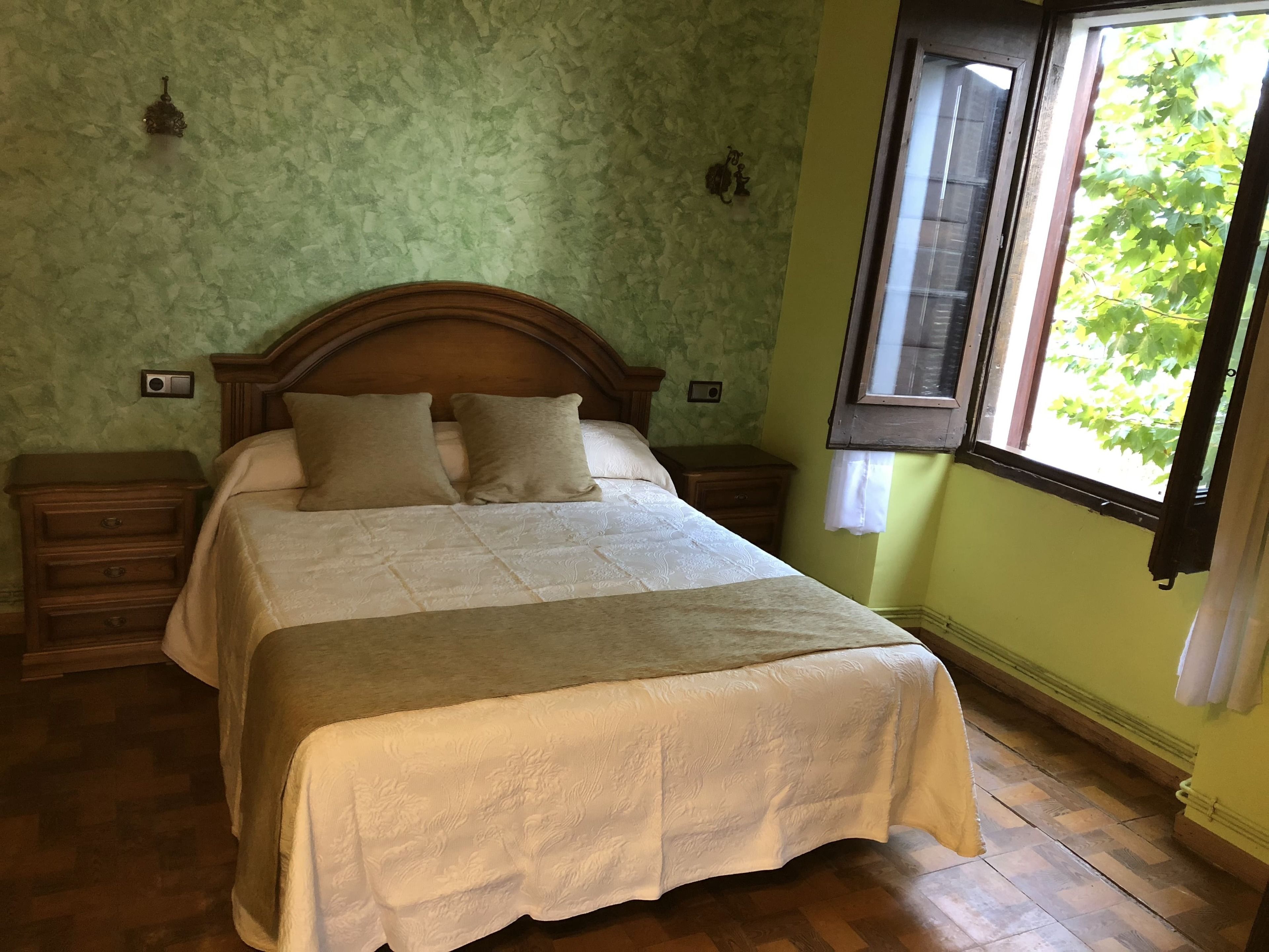 Une chambre à coucher avec un lit en bois, deux tables de chevet, une fenêtre avec des volets et un mur vert à texture.