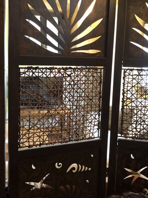 A decorative metal partition with intricate cut-out patterns and a view of an outdoor area.
