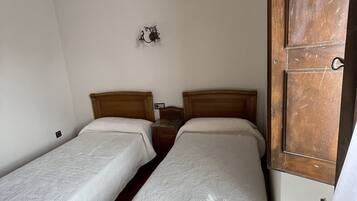Una habitación con dos camas individuales, techo de madera, una lámpara pequeña en la pared y una puerta de madera.