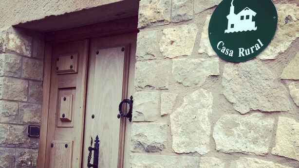 Edificio de piedra rústica con puerta de madera y un cartel que indica 'Casa Rural'.