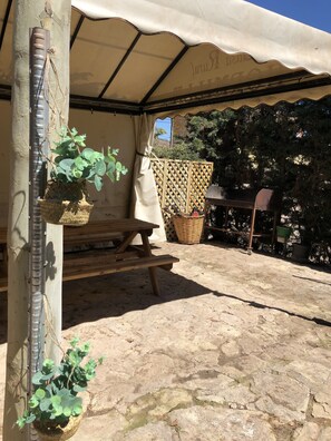 A covered outdoor area with a wooden table, a hanging plant, and a wicker basket.