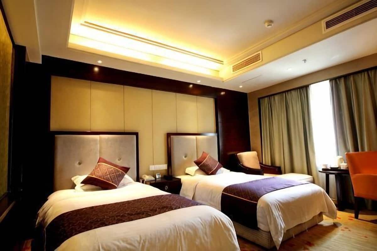 A hotel room with two beds, a desk, a chair, and a large window with curtains.