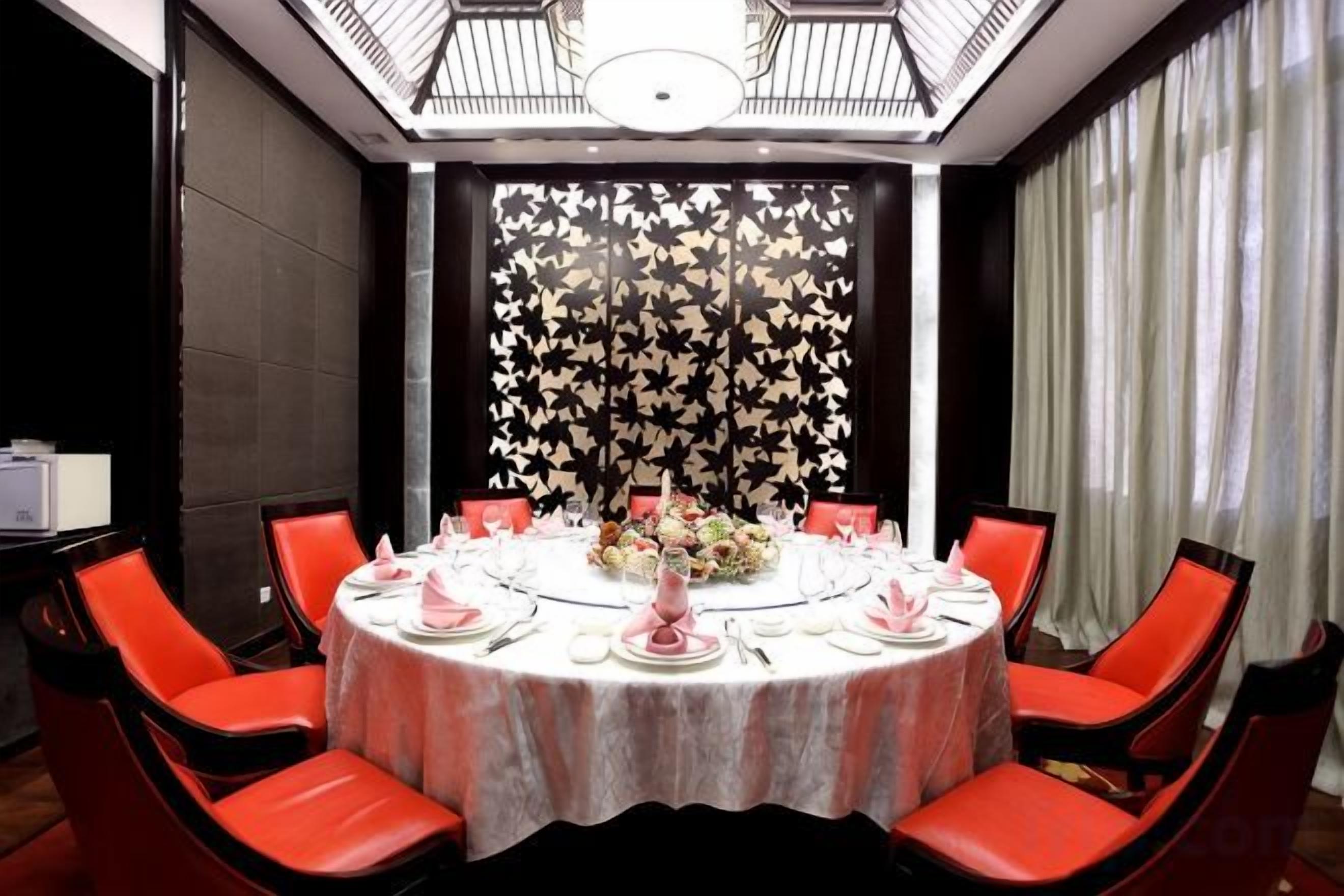Una mesa de comedor redonda con sillas rojas, un centro de mesa floral y un fondo con estampado blanco y negro.