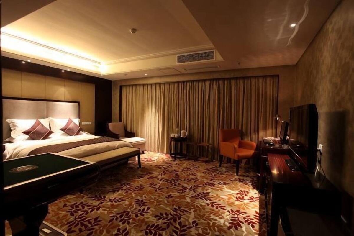 A hotel room with a bed, a desk, a chair, a television, and a carpeted floor.