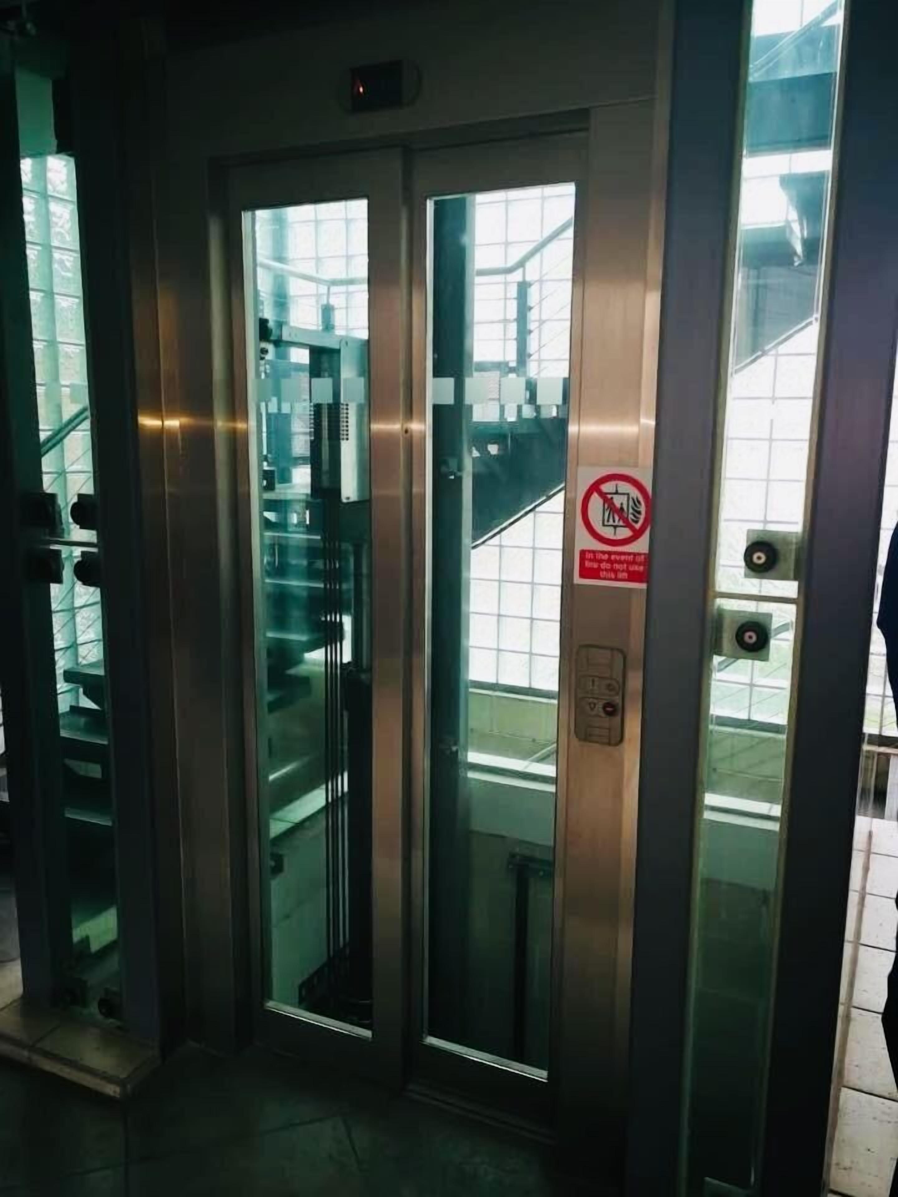 An elevator with glass doors, a no-smoking sign, and a control panel.