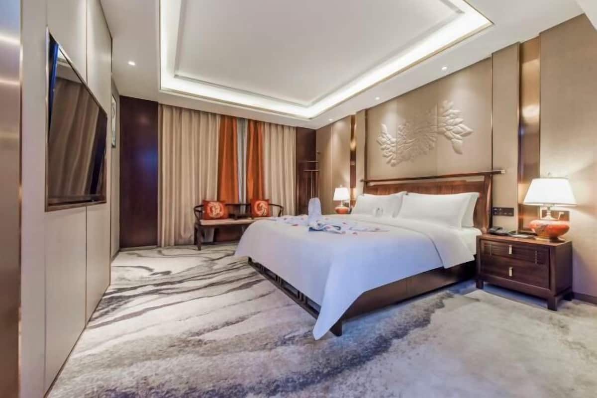 A modern hotel room with a large bed, a nightstand, a wall-mounted TV, and a decorative wall piece.