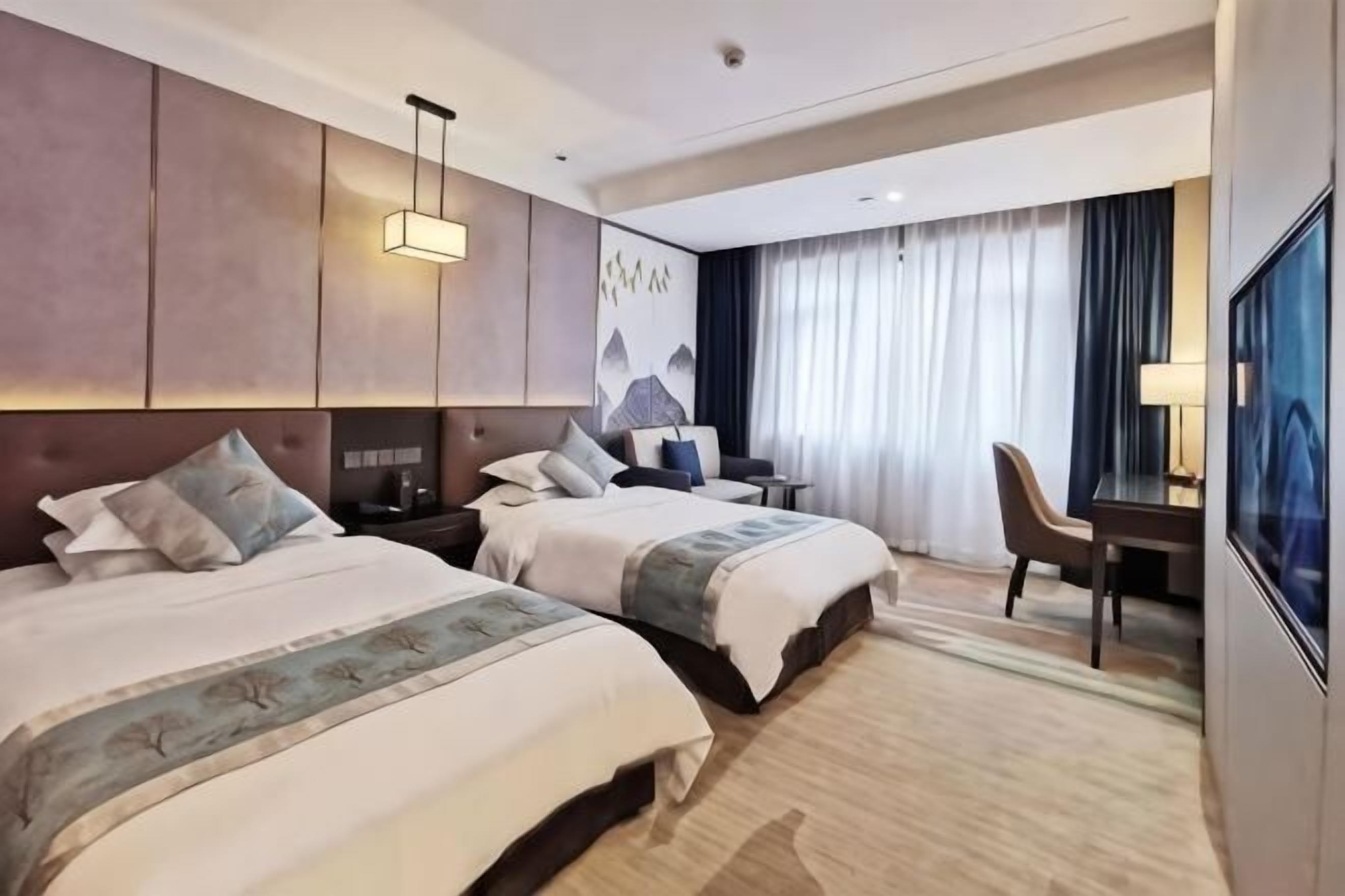 Ein Hotelzimmer mit zwei Betten, einem Schreibtisch, einem Stuhl, einem Fernseher und einem großen Fenster mit Vorhängen.