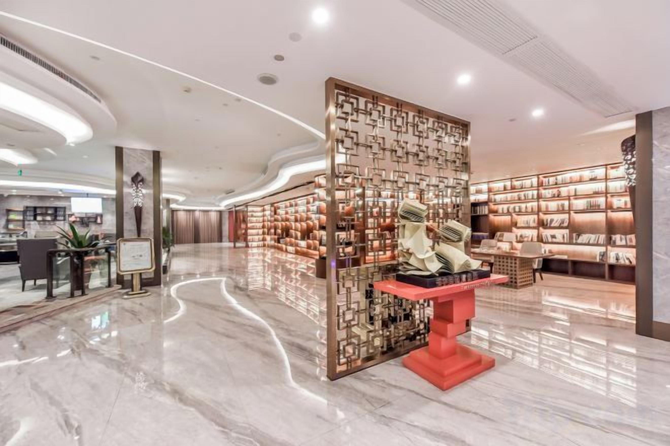 A spacious lobby with a central display, a seating area, and a wall of bookshelves.