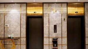 A modern elevator area with marble walls, gold accents, and a digital display. - San Xia Feng Hotel (Yunyang County)