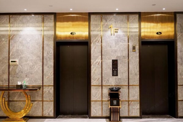 A modern elevator area with marble walls, gold accents, and a digital display.