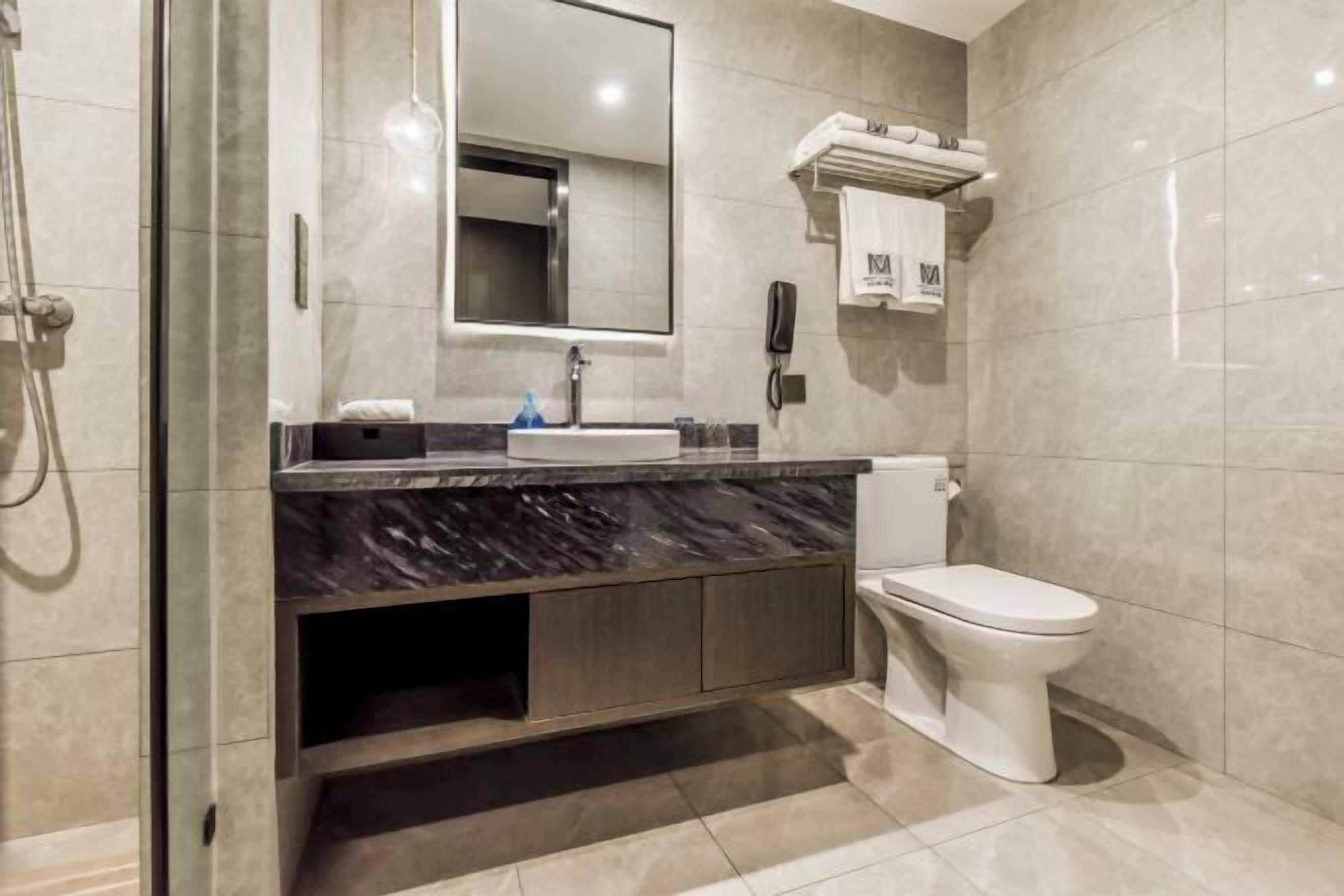 A modern bathroom with a marble sink, a toilet, and a glass-enclosed shower.