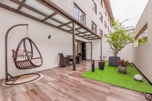 A modern outdoor patio with a hanging chair, a dining area, and potted plants.