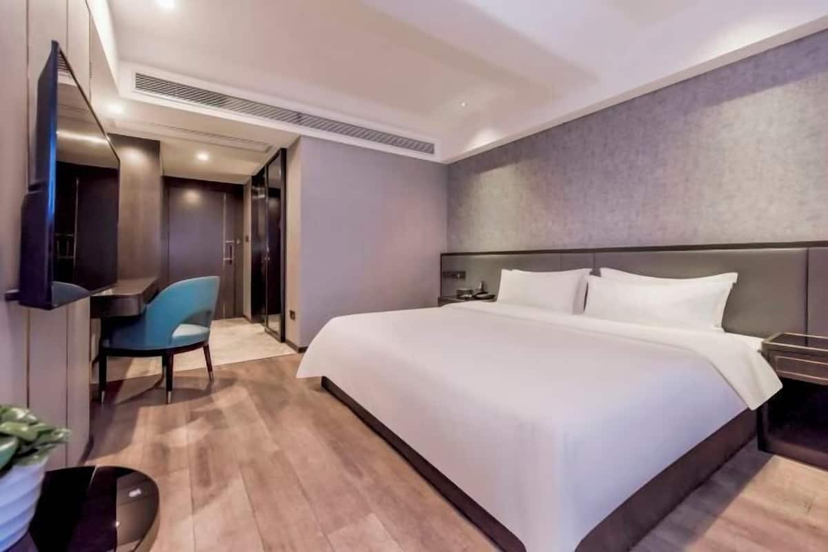 A modern hotel room with a large bed, a desk with a chair, a flat-screen TV, and a walk-in closet.