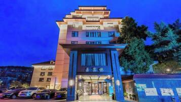 A multi-story hotel with a prominent entrance, a parking lot, and a landscaped area with trees.