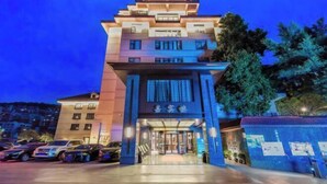 A modern hotel with a multi-story structure, a well-lit entrance, and a parking area with several cars. - San Xia Feng Hotel (Yunyang County)