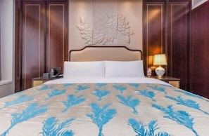 A hotel room with a large bed, a wooden headboard, a nightstand with a lamp, and a wall-mounted decorative panel.