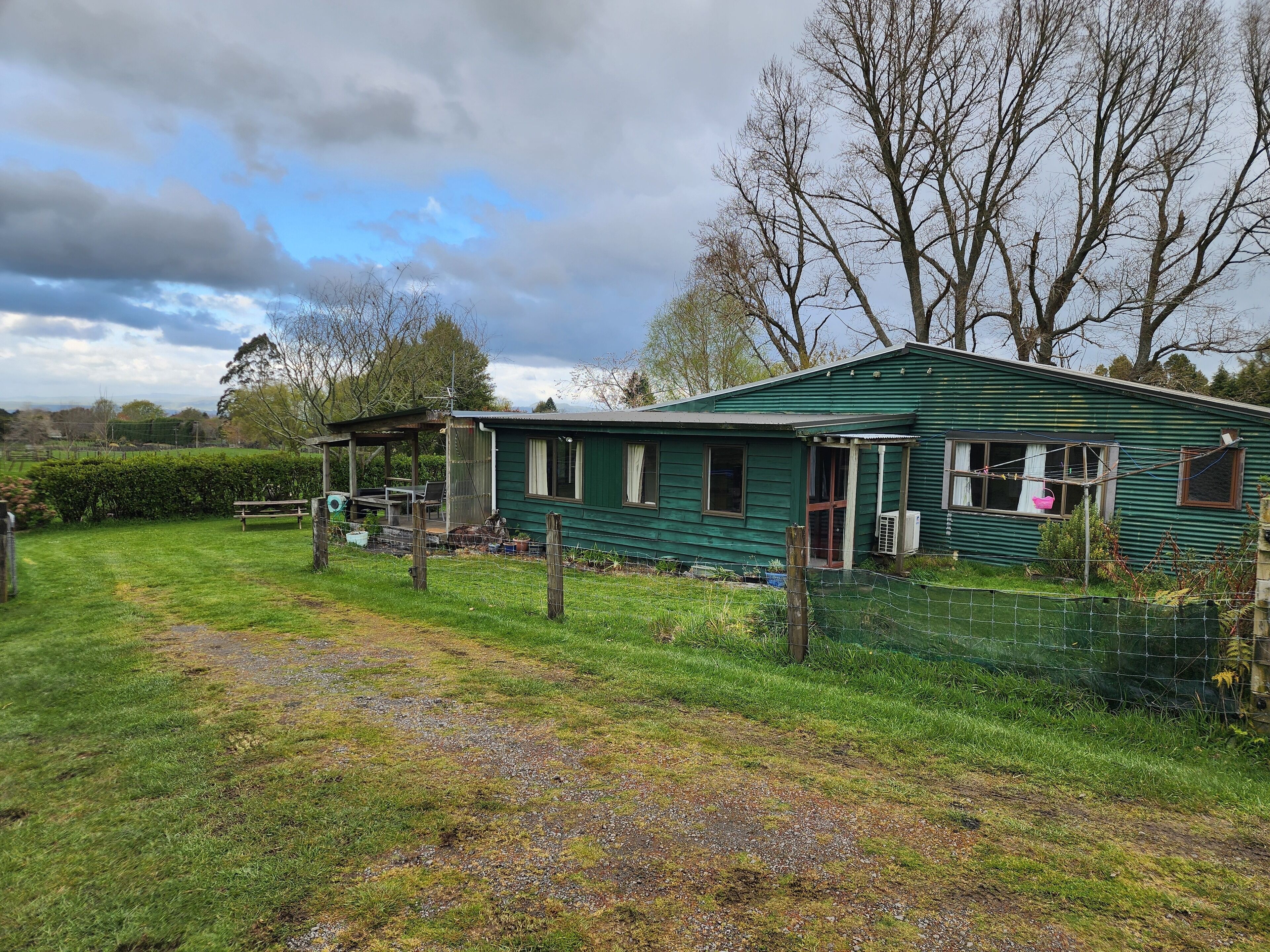 A green house with a porch, a fenced yard, and a gravel path.
