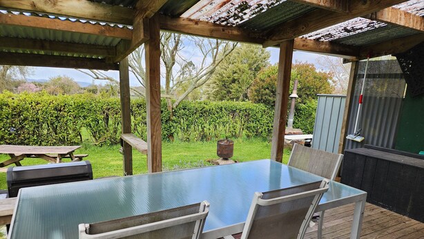 Een overdekt terras met een tafel met glazen blad en metalen stoelen.