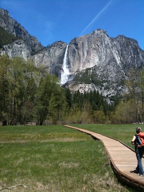 A wooden boardwalk leading to a waterfall with a rocky mountain backdrop.